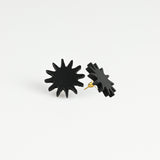 A pair of black starburst stud earrings with gold-tone posts, shown on a clean white background.