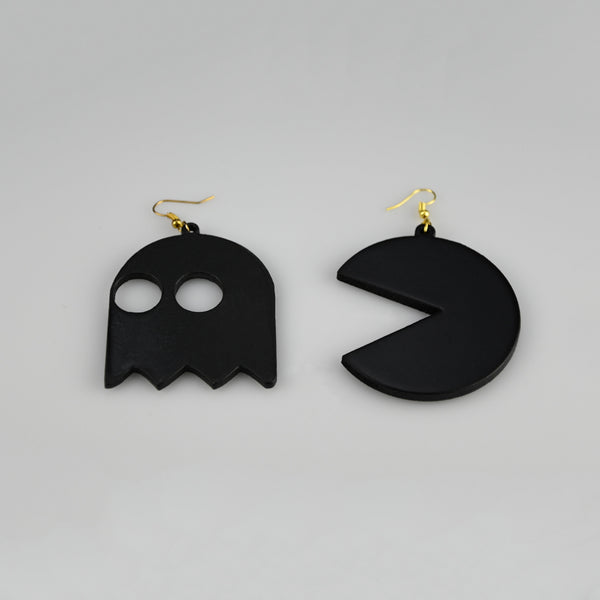 A pair of black dangling earrings shaped like a ghost and a Pac-Man style circle, each with a gold fishhook ear wire, photographed on a plain light gray background.