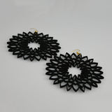 A pair of black laser-cut dangle earrings with a geometric, sunburst-like pattern and small gold fishhook wires, displayed on a light gray background.